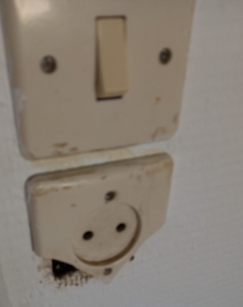 Prise électrique murale cassée avec fils apparents remise en conformité par Rapido Travaux – réparation et sécurisation d’installation électrique.